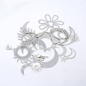 May include: A collection of silver metal charms featuring various celestial designs, including moons, stars, suns, and a flower. The charms are ideal for jewellery making or crafting projects.