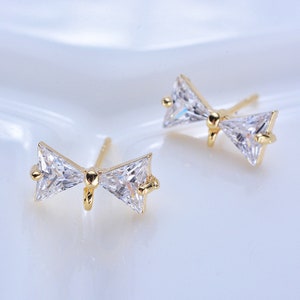 May include: A pair of gold bow-shaped earrings with clear cubic zirconia stones.