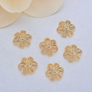 May include: Six gold-colored metal flower-shaped bead caps. The bead caps have a delicate, intricate design.