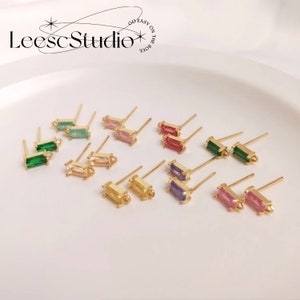 May include: A set of 10 pairs of gold-tone stud earrings with rectangular shaped gemstones in various colors, including green, pink, red, purple, and yellow. The earrings are displayed on a white surface.  Go Easy on the Soul.