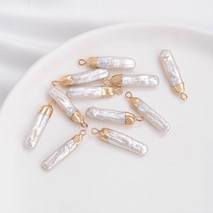 May include: A group of ten white pearl and gold pendant charms. The charms are shaped like long, thin rectangles with a gold cap on one end and a loop on the other.