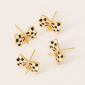 May include: Four gold-toned earring findings with a black and white checkered bow design. Each bow has a clear rhinestone in the center.