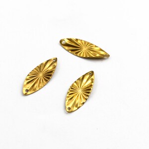 May include: Three gold-coloured metal leaf-shaped embellishments with a starburst design. Each leaf has two holes for attaching to a project.