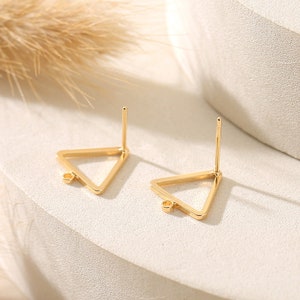 May include: Two gold triangle earring settings with a loop at the bottom and a post on the top.