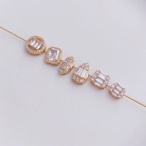 May include: A set of six gold-tone jewelry charms featuring different geometric shapes, each adorned with clear cubic zirconia stones.