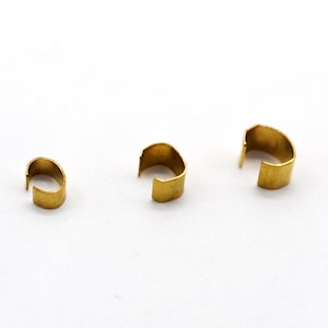 Op de afbeelding: Drie gouden metalen ringen, elk met een andere maat, zijn in een rij op een wit oppervlak gerangschikt.