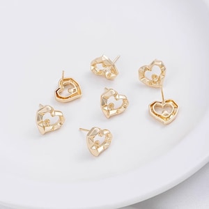 May include: Six gold-tone heart-shaped earring settings with a small hole in the centre of each heart. The settings are designed with a textured, faceted surface.