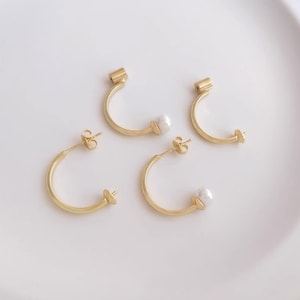 Puede incluir: Un par de pendientes de aro dorados con un acento de perla. Los pendientes están hechos de un metal fino y delicado y tienen un diseño simple y elegante.