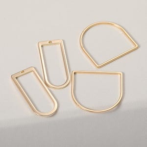May include: Four gold-colored metal jewelry findings in various geometric shapes: a rectangle, a rounded rectangle, a half-circle, and a teardrop shape. Each piece has a small hole for attaching to other components.
