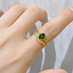 Può includere: Un anello d'oro con una pietra ovale verde e un design a catena. L'anello è incastonato con piccole pietre chiare.