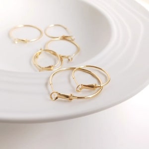 May include: Four gold hoop earrings with a clasp closure. The earrings are on a white surface.