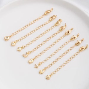 May include: Eight gold extender chains with different charms, including a teardrop, heart, flower, crescent moon, teardrop, star, hand, and flower. Each chain has a lobster clasp.
