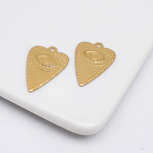 Puede incluir: Dos abalorios de corazón de color dorado con un diseño de ojo en relieve. Los abalorios tienen una superficie texturizada y son perfectos para la elaboración de joyas.
