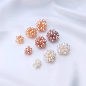 May include: Assortment of pearl clusters in various sizes and shades of pink, white, and cream. The pearls are clustered together to form small, round shapes.