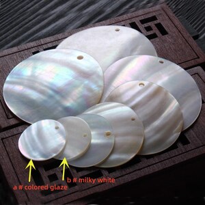 May include: Assortment of round, white mother of pearl shell discs with holes for hanging. Some discs have a milky white color, while others have a colored glaze.