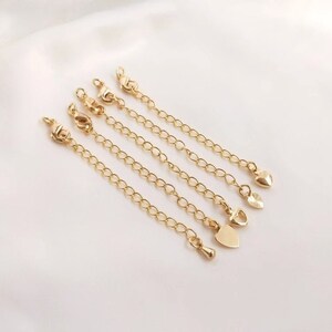 May include: Five gold chain extenders with different heart-shaped charms. The extenders are made of a delicate chain and are perfect for adding a touch of elegance to necklaces.