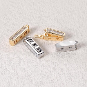 May include: A collection of rectangular jewelry clasps featuring clear stones set in gold and silver-toned metal. The set includes two gold-toned clasps with embedded stones, one silver-toned clasp with stones, and one plain silver-toned clasp component.