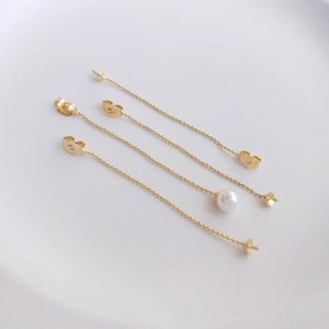 May include: Four gold earring chains with a single pearl charm on one chain. The chains are all different lengths.
