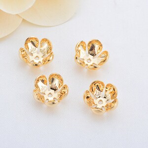 May include: Four gold-colored metal flower-shaped bead caps. The caps have a five-petal design with a small hole in the center.