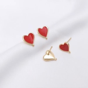 May include: A pair of gold heart-shaped earrings with red enamel. One pair has a gold post and the other has a gold hook.