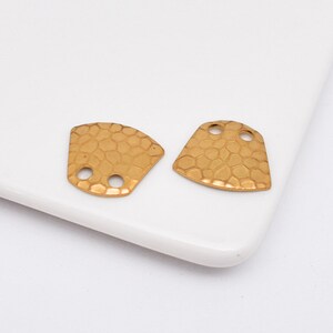 May include: Two gold-toned metal connector pieces with a textured surface and two holes each. The pieces are shaped like a slightly rounded triangle.