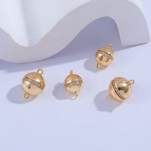 May include: Four gold-toned magnetic clasps with clear crystal accents. Each clasp has two loops for attaching jewelry.