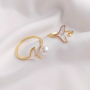 May include: Two gold rings with white mermaid tail designs. One ring has a pearl accent.