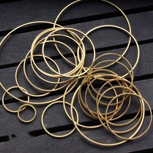May include: A collection of gold-toned metal hoops of varying sizes, arranged in a random pattern on a dark wooden surface.