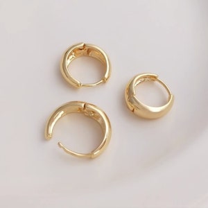 May include: Three gold hoop earrings, each with a smooth, rounded surface. The earrings are arranged on a white background.