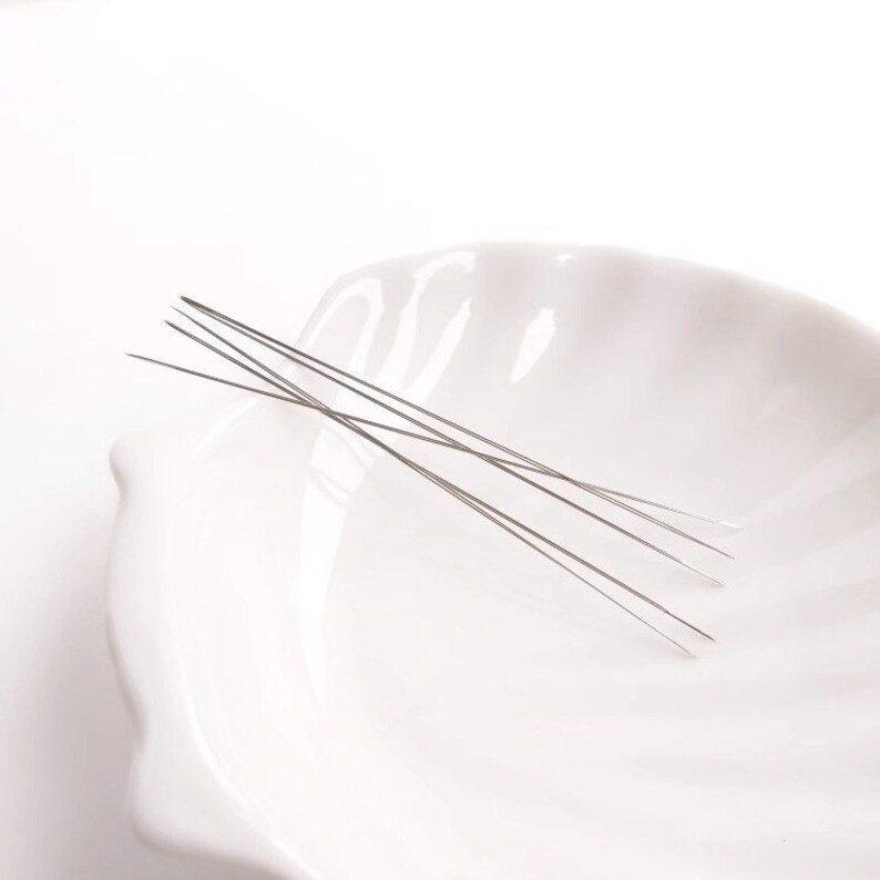 May include: A set of five thin, silver-colored needles in a white ceramic bowl.