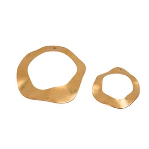 Pode incluir: Dois anéis de metal de cor dourada com uma forma irregular e ondulada. Os anéis têm um furo na parte superior para pendurar.