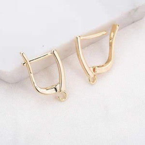 May include: Two gold-toned earring hooks with a simple, open design. The hooks are made of metal and have a smooth finish.