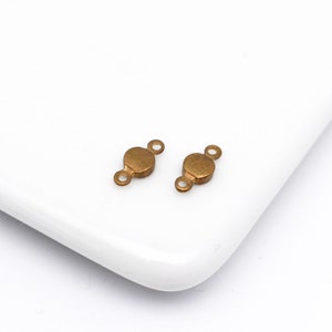 May include: Two antique gold-toned metal connector pieces with two loops on each side. The connector pieces are round and have a slightly textured surface.