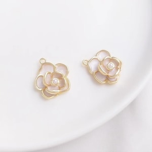May include: Two gold-tone flower charms with a white pearl center. The flowers have a pink enamel finish.