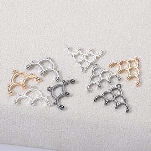 May include: A collection of metal jewelry findings in various colors, including gold, silver, and gunmetal. The findings have a decorative, curved design with multiple loops, suitable for crafting necklaces, bracelets, and earrings. The pieces are arranged on a light-colored surface.