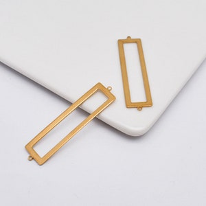 May include: Two gold-toned metal rectangular frames with open centers and jump rings at the top and bottom.