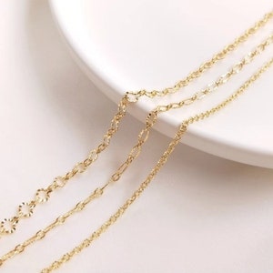 May include: Three gold chains of different lengths and styles. The chains are layered on top of each other and are on a white background.