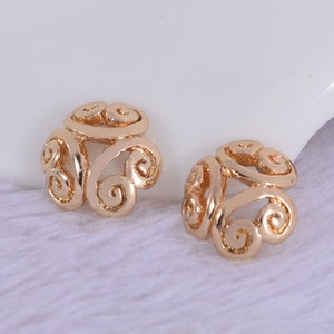May include: A pair of gold-tone earrings with a delicate, intricate design featuring swirling patterns. The earrings are small and lightweight, making them a perfect choice for everyday wear.