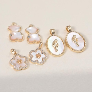 May include: A collection of gold-toned pendants featuring various designs. The pendants include bear shapes, flower shapes with clear crystals, and oval pendants with a tulip design. Each pendant has a mother-of-pearl inlay.