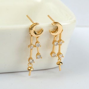 May include: A pair of gold-tone earrings with a crescent moon charm and dangling crystal accents. The earrings have a delicate, feminine design.