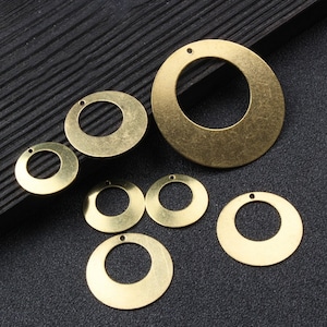 Könnte beinhalten: Sortiment aus sechs goldfarbenen Metallkreisen mit einem Loch in der Mitte. Die Kreise sind in verschiedenen Größen und auf einer schwarzen Oberfläche angeordnet.