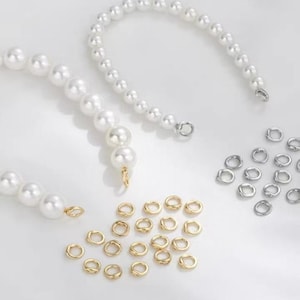 Puede incluir: Un conjunto de suministros para la fabricación de joyas, que incluye hilos de perlas blancas de imitación, anillas doradas y anillas plateadas. Las perlas están ensartadas en un alambre flexible, y las anillas son conectores pequeños y circulares.