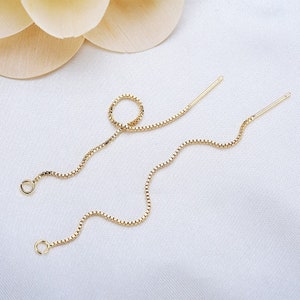 May include: A pair of gold chain earrings with a delicate box chain design. The earrings are long and dangle, with a small loop at the top and a straight post at the bottom.
