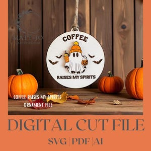 May include: A round, white wooden ornament with a ghost wearing a hat and holding a coffee cup and a lantern. The text "COFFEE RAISES MY SPIRITS" is printed on the ornament. Three orange pumpkins and fall leaves are in the background.