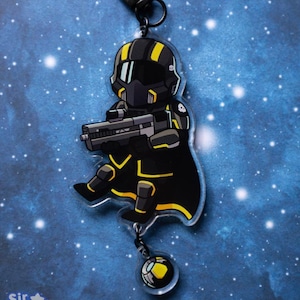 Op de afbeelding: Een zwart-gele cartoon sleutelhanger met een soldaat met een blaster. De sleutelhanger heeft een zwarte sluiting en een kleine, doorzichtige bedel met een geel en zwart ontwerp. De tekst "Sir Burnt" staat in de linker benedenhoek.