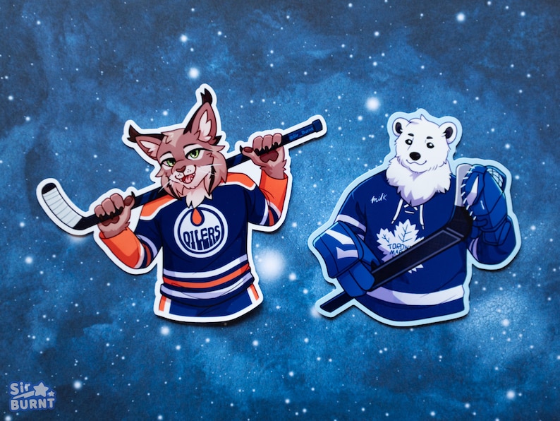 May include: Two die-cut stickers featuring anthropomorphic animals in hockey jerseys. One is a bobcat in an Oilers jersey, the other a polar bear in a Maple Leafs jersey, both holding hockey sticks. The background is a dark blue with white dots.