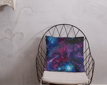 May include: A throw pillow with a watercolor galaxy design featuring shades of blue, purple, and pink. The pillow is sitting on a white chair with a black metal frame.