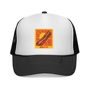 Puede incluir: Una gorra de camionero blanca y negra con un gráfico cuadrado en el panel frontal. El gráfico muestra una tira de tocino sobre un fondo de sol amarillo con el texto BACON IS LIFE impreso en letras naranjas en la parte inferior.