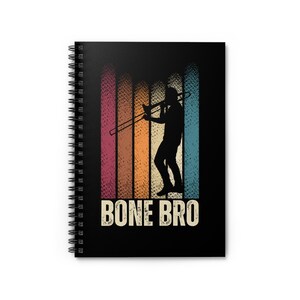 May include: A black spiral notebook with a retro-style design featuring a silhouette of a person playing a trombone. The background is a colourful striped pattern with the text "BONE BRO" in white.