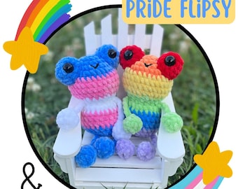 May include: Two crocheted frog plushies sitting on a white bench. The frog on the left is blue, pink, and white, and the frog on the right is rainbow colored. The text "PRIDE FLIPSY & TRANS PRIDE FLIPSY" is visible in the image.